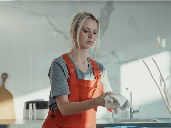 A cleaner in work overalls wiping down a kitchen worktop