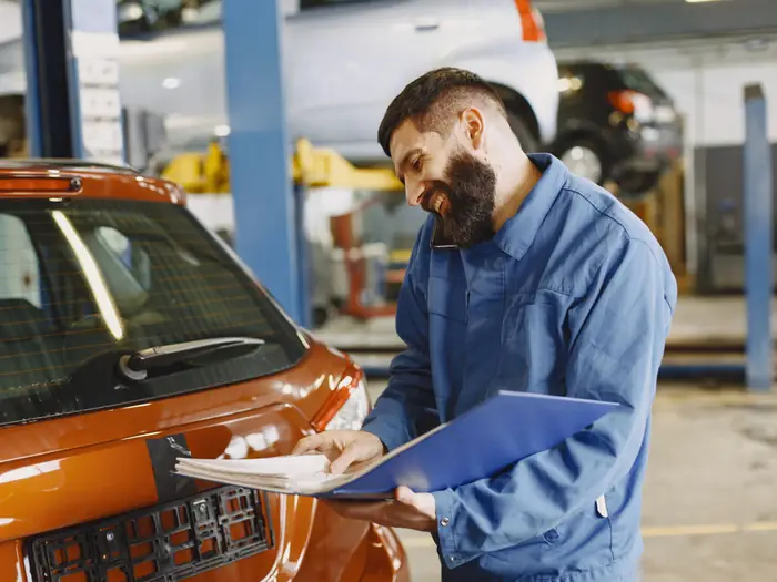 A mechanic in overalls checking a car over on the ramp in a service garage