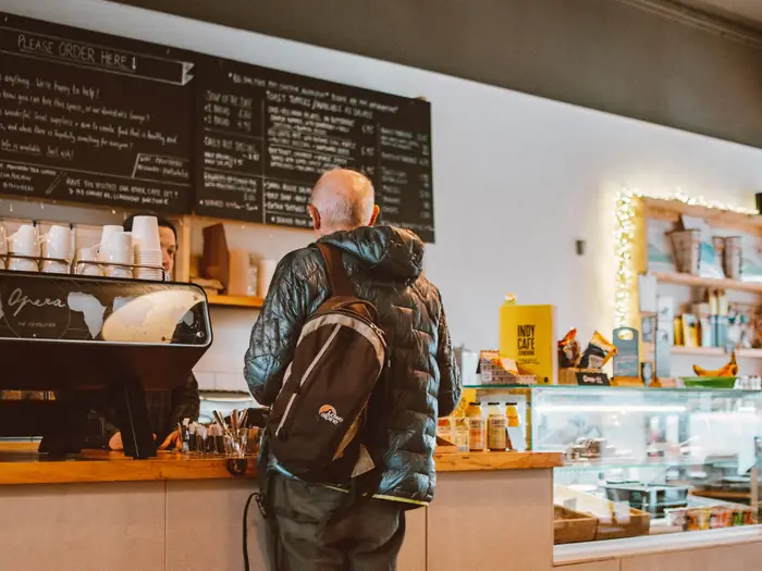 A customer ordering at the counter of a small café under a chalkboard menu